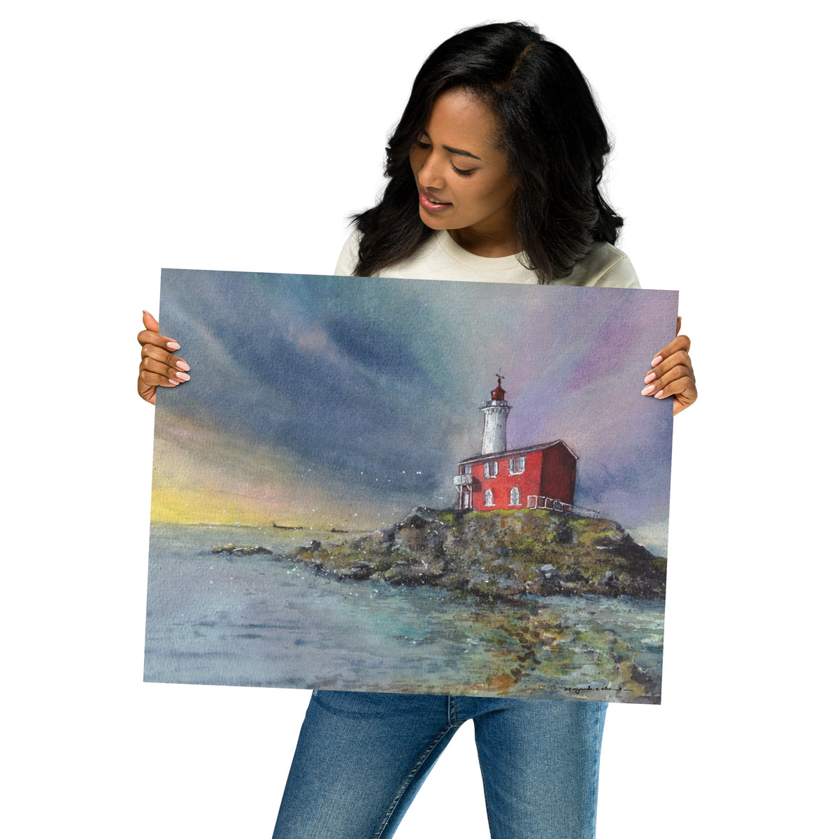 Model in a light top holding the unframed Fisgard Lighthouse print at an angle; Fisgard Lighthouse on a rocky shoreline beneath a dramatic blue, violet and yellow sky, with the red keeper's house reflected in calm coastal water.