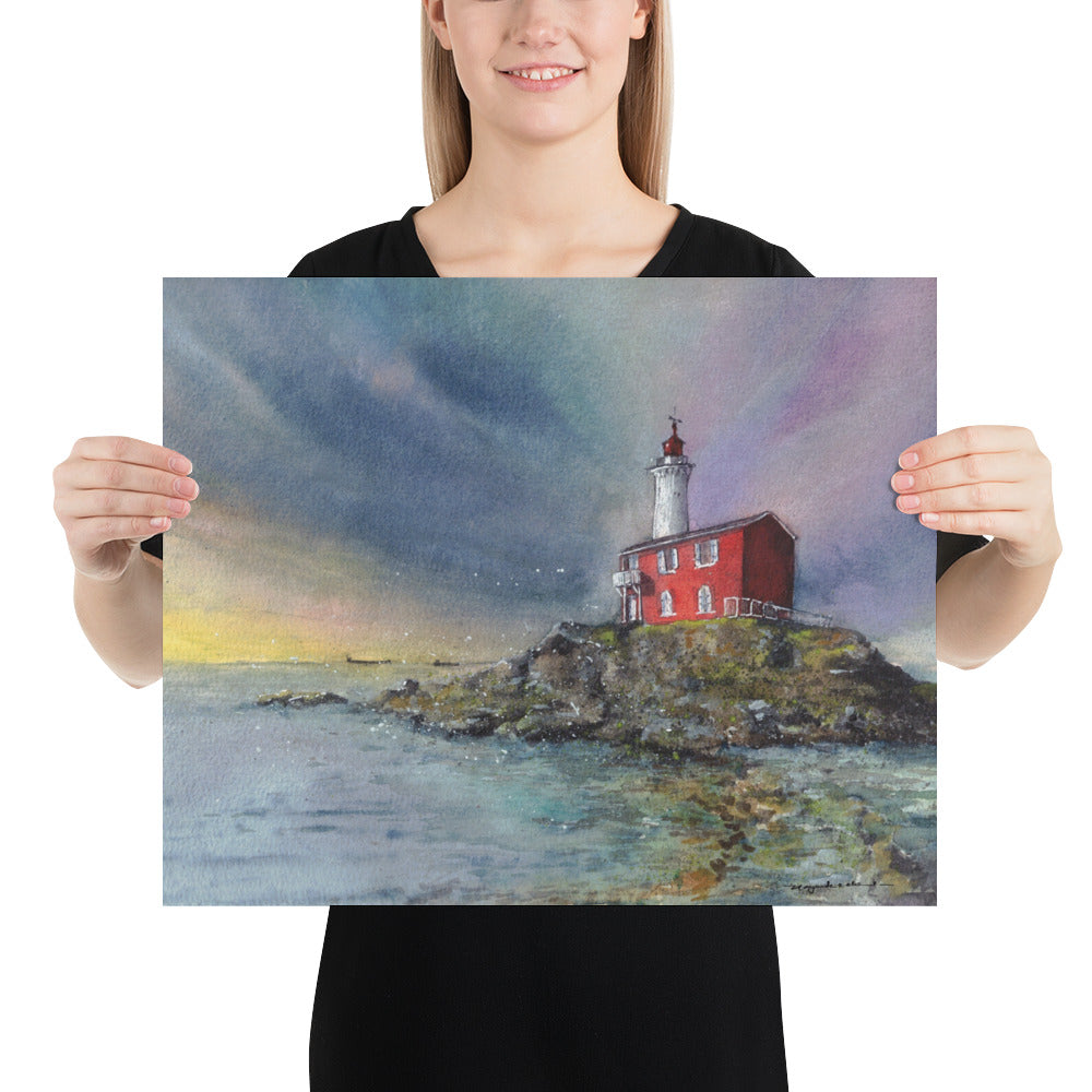 Model in a black top holding the unframed Fisgard Lighthouse landscape print; Fisgard Lighthouse on a rocky shoreline beneath a dramatic blue, violet and yellow sky, with the red keeper's house reflected in calm coastal water.